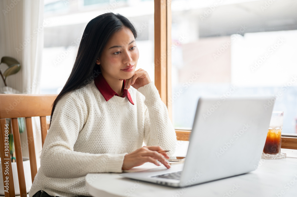 Asian woman is looking intently at laptop screen, with one hand under chin and other holding pencil. Asian woman is looking intently at laptop screen, with one hand under chin and other holding pencil.