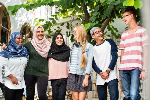 Diverse group of friends laughing outdoors. Friends of various ethnicities enjoying time together. Smiling friends in casual attire under a tree. Diverse friends hanging out together.