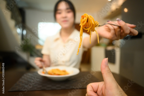 Young woman offering a forkful of spaghetti to her husband across the table with thumbs up photo