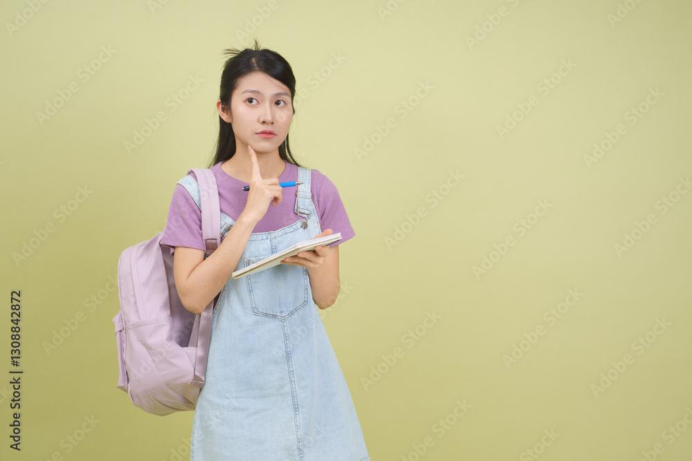 Student holding a notebook with a thoughtful expression, standing against a plain green background Student holding a notebook with a thoughtful expression, standing against a plain green background
