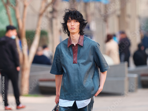 Portrait of handsome Chinese young man wearing short sleeved shirt and shorts posing in the street, young guy with black curly hair with urban background. male fashion, cool Asian young man lifestyle