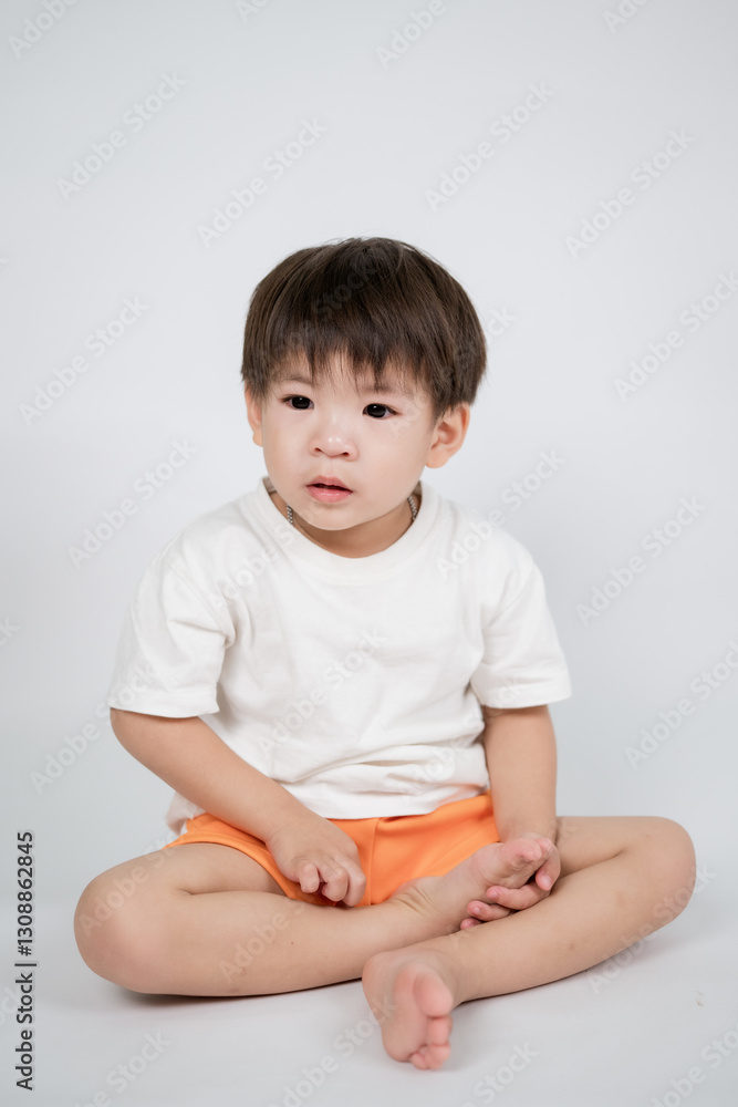 young child with short hair sits cross legged on floor, wearing white t shirt and orange shorts, against plain background. child appears calm and focused young child with short hair sits cross legged on floor, wearing white t shirt and orange shorts, against plain background. child appears calm and focused