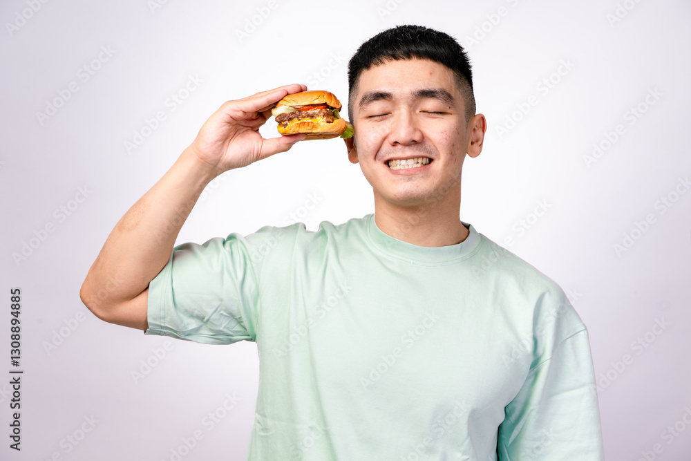 An Asian man in a mint green shirt is about to take a big bite of a cheeseburger. He has an excited expression. The background is white An Asian man in a mint green shirt is about to take a big bite of a cheeseburger. He has an excited expression. The background is white
