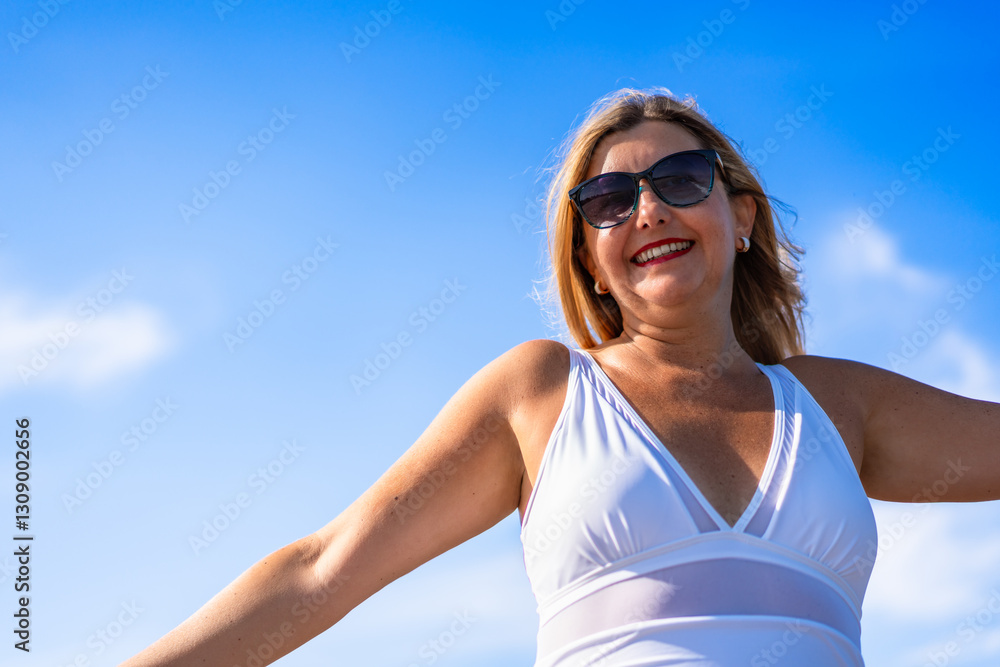 Portrait of beautiful happy middle aged woman in swimsuit standing against background of blue sky in summertime Portrait of beautiful happy middle aged woman in swimsuit standing against background of blue sky in summertime