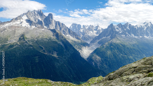 Majestic mountain range with rugged peaks, green valleys, and a bright blue sky with scattered clouds in the French Alps