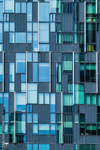 A cropped view of an apartment facade features a modern pattern of square and rectangular blue and green tinted glass windows, creating a striking geometric design