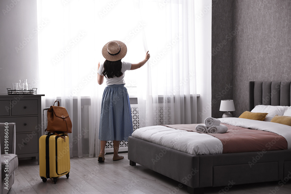 Fototapeta premium Traveller with suitcase opening curtains in hotel room, back view