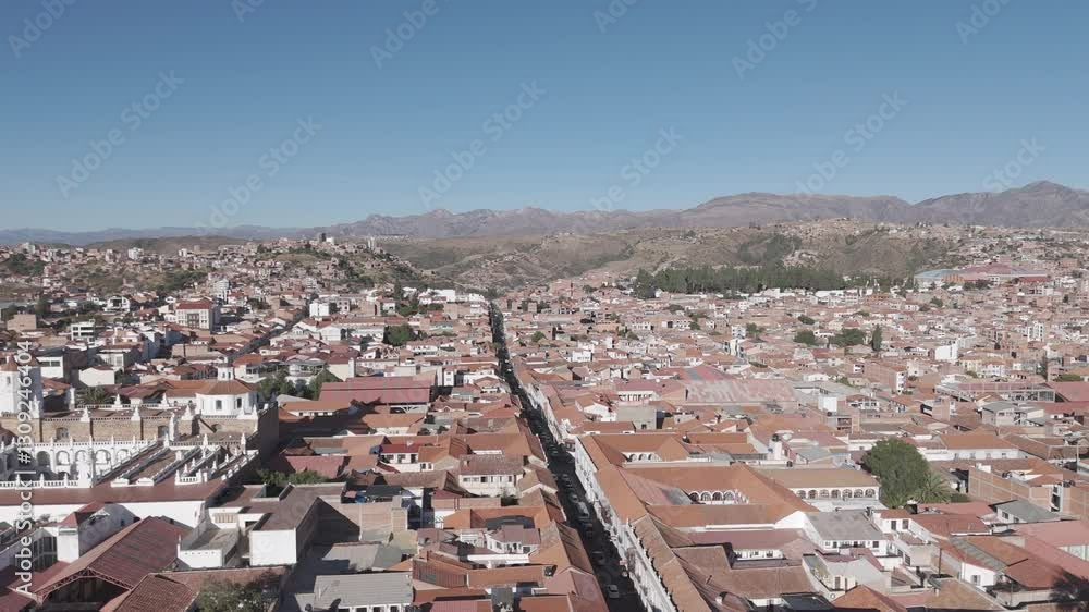 Wide drone shot of Sucre Bolivia on a bright day with blue sky with small hills in the background LOG