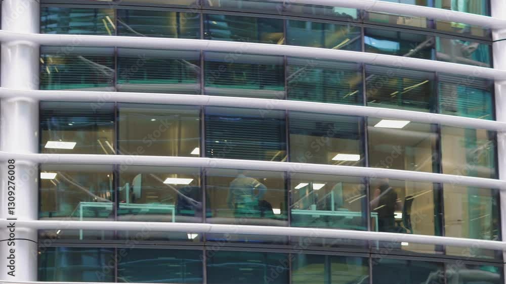 Office windows in a modern glass skyscraper with employees at their desks Office windows in a modern glass skyscraper with employees at their desks