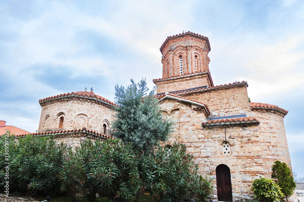 Fototapeta premium Magnificent St. Naum Monastery, along Ohrid lake, in Byzantine architecture, Eastern Orthodox monastery, with traditional stone architecture and red rooftops, moody sky.