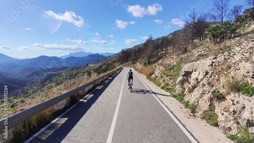 Cyclist rides along a scenic asphalt road winding through a beautiful landscape under a partly cloudy sky. Perfect for travel, adventure, and active lifestyle themes. Costa Blanca, Spain