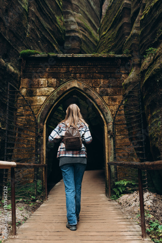 A tourist woman with a backpack stands against the background of a rocks. Young 30s blonde woman hiking in nature. Concept of an active lifestyle. High quality photo. Full body, rear view