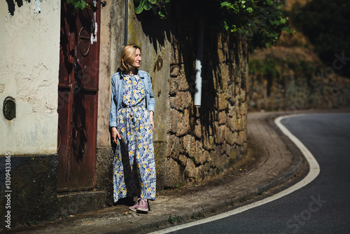 Obraz na płótnie A woman in a light dress stands near a road in a picturesque Portuguese village, exuding charm and simplicity. w salonie