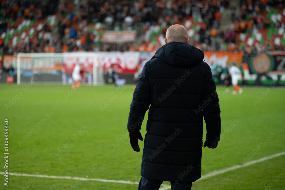 Head coach's back and soccer match at the stadium in the background.