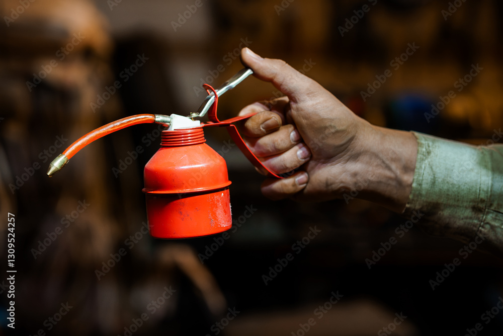 Close-up of Hand Holding Red Oil Can in Mechanical Workshop Environment Close-up of Hand Holding Red Oil Can in Mechanical Workshop Environment