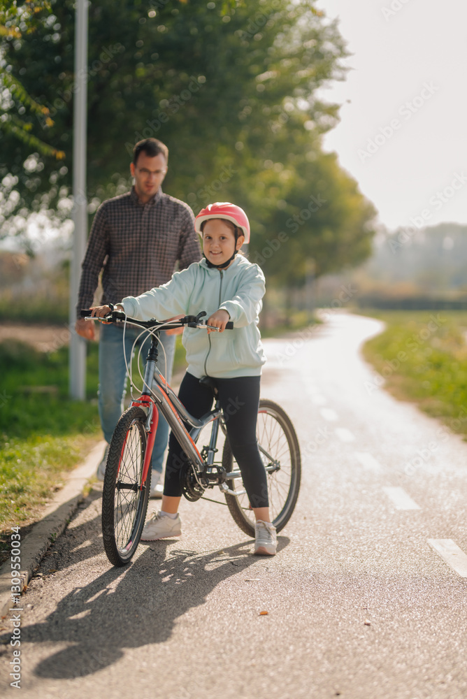 Father watching daughter learning to ride bicycle in park Father watching daughter learning to ride bicycle in park