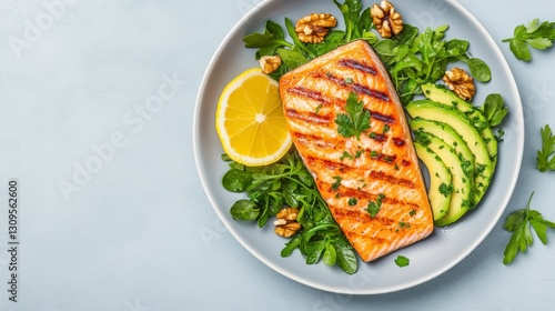 Grilled salmon fillet served with fresh greens, avocado slices, lemon, and walnuts on a light blue background.