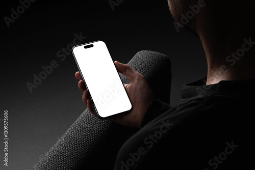 A man in a dark outfit holding smartphone against a dark gray background.Isolated blank mockup surface to place your design. 