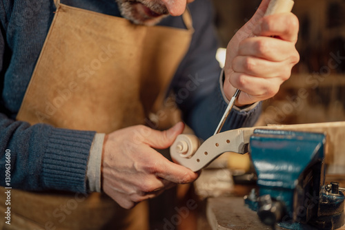 Luthier working on violin scroll using gouge and vise in workshop