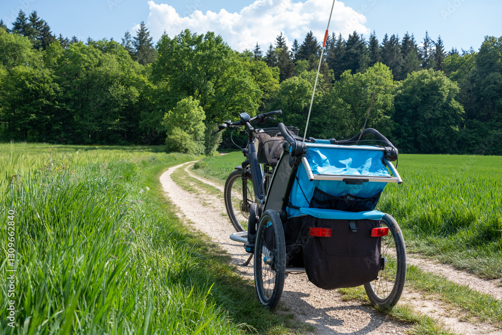 A bicycle with a child trailer parked on a winding dirt path through lush green fields, surrounded by nature and adventure. A bicycle with a child trailer parked on a winding dirt path through lush green fields, surrounded by nature and adventure.