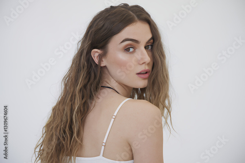 a beautiful woman posing gracefully, looking over her shoulder. She has long, wavy hair, and a captivating expression. The image focuses on her elegant features and confident demeanor