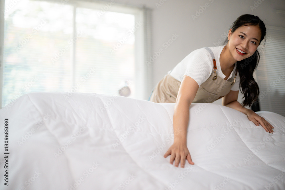 Smiling maid arranging a white duvet on a bed in a hotel room Smiling maid arranging a white duvet on a bed in a hotel room