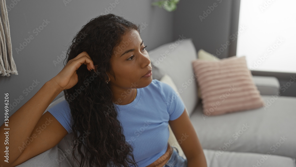 Young hispanic woman relaxing in a modern living room, sitting on a comfortable couch with a thoughtful expression, indoor setting in an apartment Young hispanic woman relaxing in a modern living room, sitting on a comfortable couch with a thoughtful expression, indoor setting in an apartment