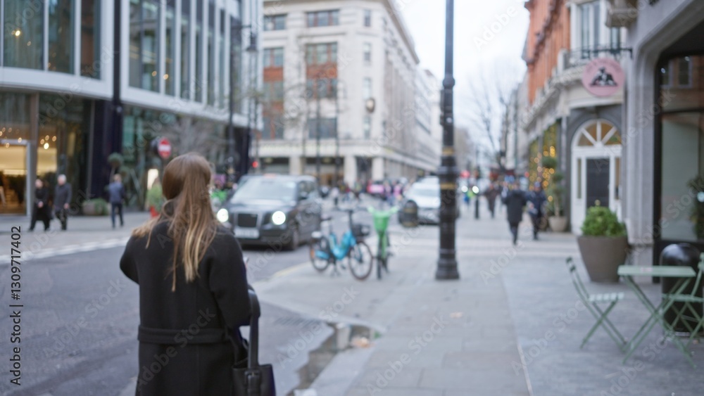 Obraz premium Woman walking on a busy london street during winter with blurred cars, pedestrians, and buildings in the background, capturing the essence of urban life in england.