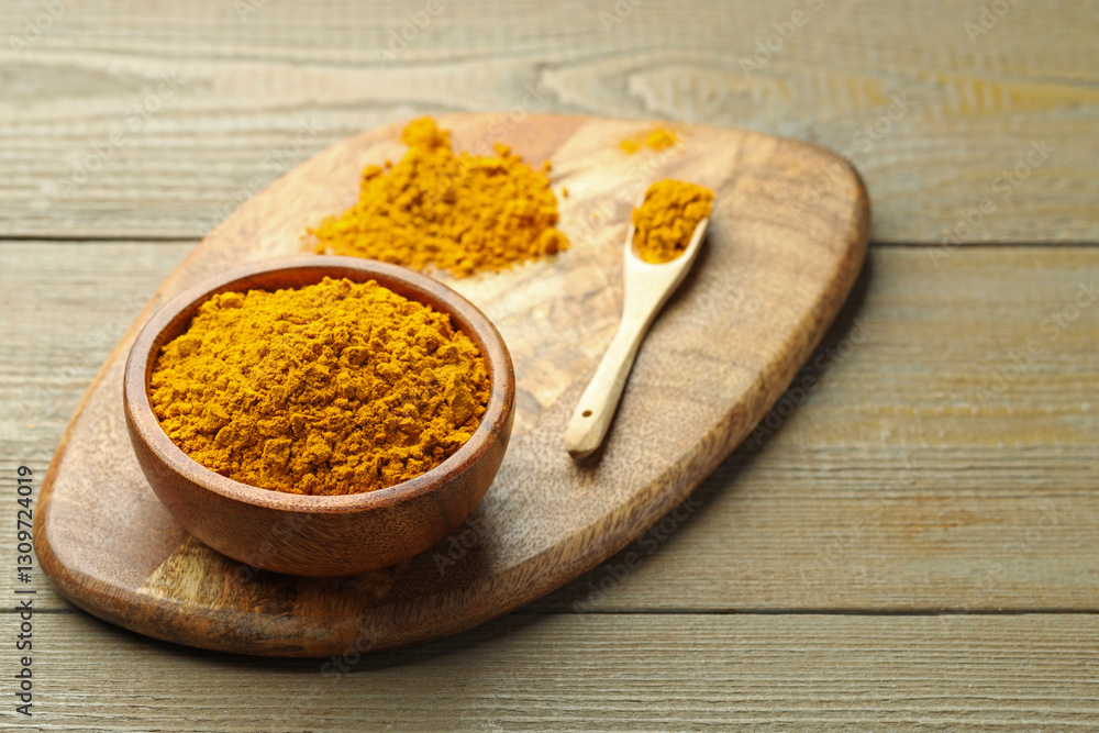Turmeric powder in bowl and spoon on wooden table, closeup Turmeric powder in bowl and spoon on wooden table, closeup