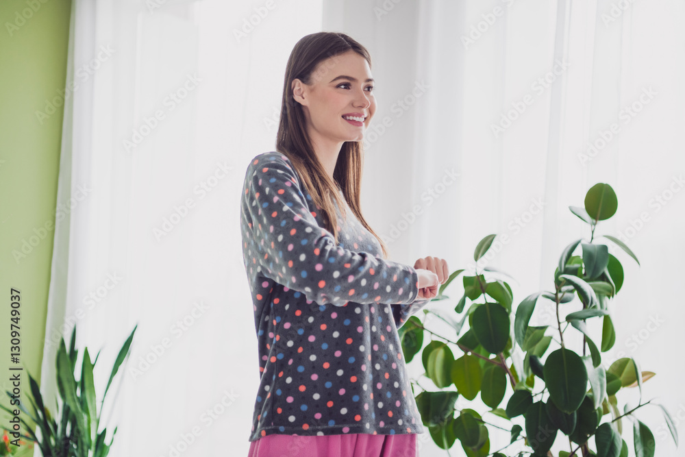 Smiling young woman in comfortable pajamas indoors near green houseplants enjoying a relaxing morning at home. Smiling young woman in comfortable pajamas indoors near green houseplants enjoying a relaxing morning at home.