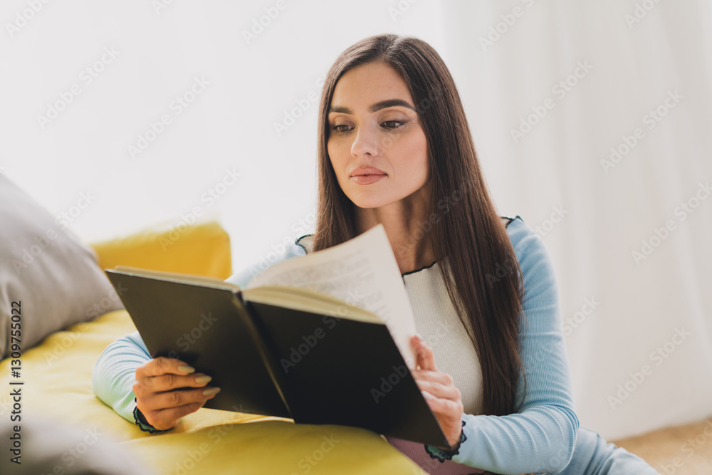 Young brunette woman sitting indoors and enjoying a quiet moment while reading a book under soft daylight in a cozy home setting. Young brunette woman sitting indoors and enjoying a quiet moment while reading a book under soft daylight in a cozy home setting.