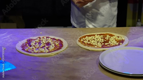 Overhead timelapse: hands spread tomato sauce and place cheese on two pizza doughs. Close-up cooking process, ideal for food ads, recipes, culinary content. Neutral backdrop, no faces, loopable.