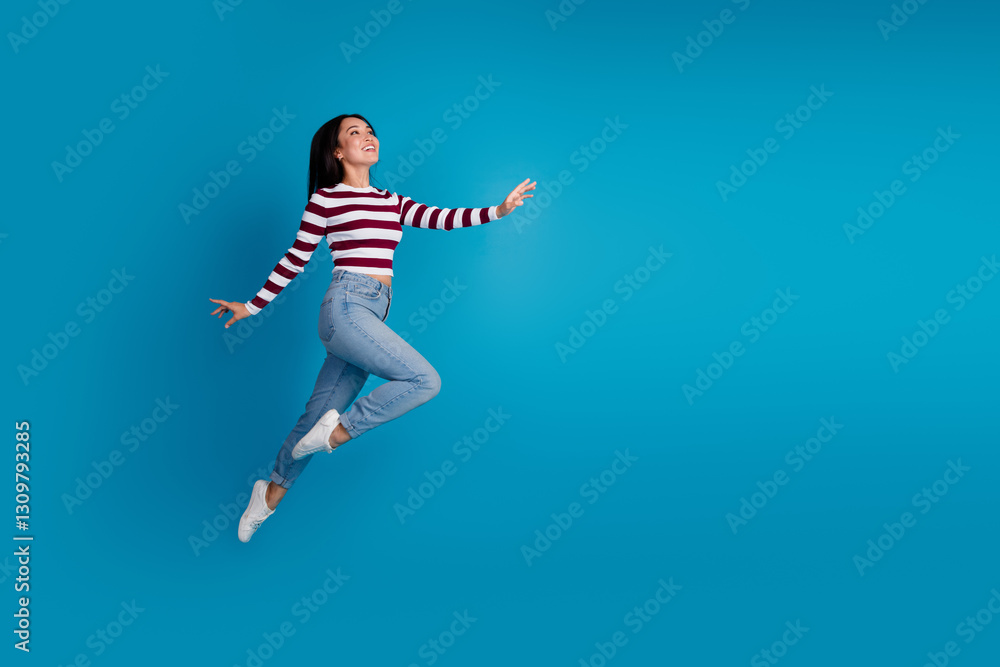 Smiling young woman leaping with joy against a solid blue background wearing trendy casual striped shirt and jeans Smiling young woman leaping with joy against a solid blue background wearing trendy casual striped shirt and jeans