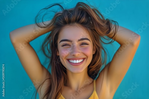 Young Woman Smiles Joyfully Against a Vibrant Blue Background in Bright, Sunl...