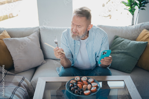 Εκτύπωση καμβά Elderly man enjoying sushi with a smartphone at home, deciding between chopstick