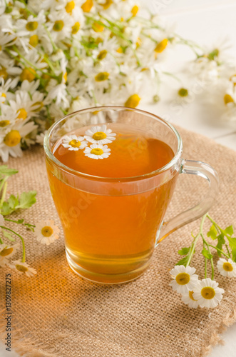 Chamomile tea in a transparent cup on a white wooden background with a bouquet of daisies with selective focus