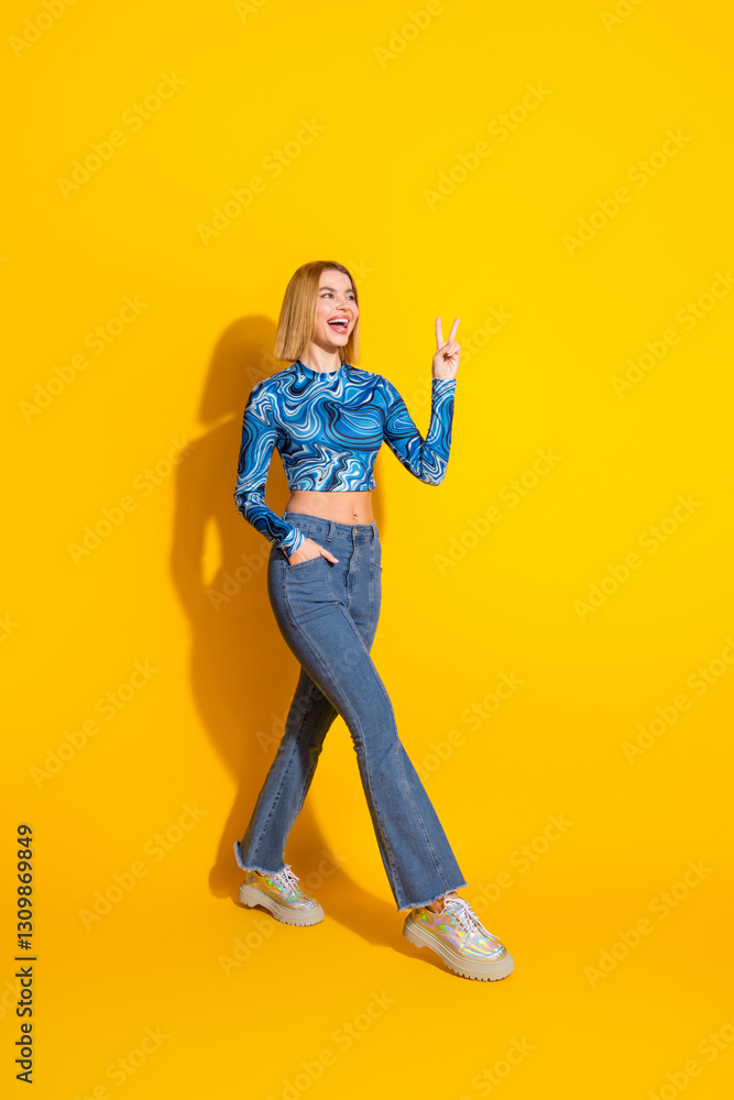 Young stylish woman gesturing peace sign on vibrant yellow vertical backdrop, showcasing casual fashion with playful charm Young stylish woman gesturing peace sign on vibrant yellow vertical backdrop, showcasing casual fashion with playful charm
