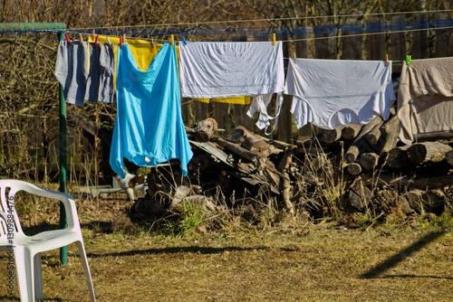 Laundry is drying on a clothesline in the countryside. A white plastic chair stands next to the clothesline.Washed laundry on a clothesline.T-shirts and socks are dried in the sun.