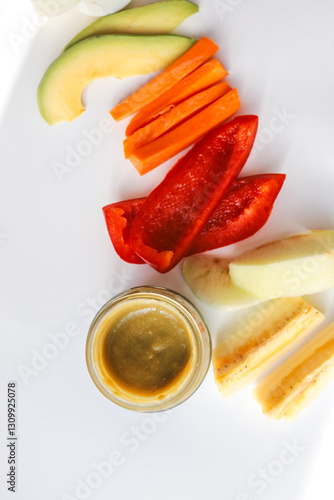 A glass jar of homemade baby puree with fresh vegetables and fruits arranged on a white background. Includes carrot, bell pepper, apple, and banana. Healthy organic food for infants and toddlers