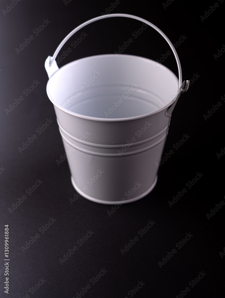 A high-contrast photograph showcasing a minimalistic white metal bucket against a dark background, perfect for home organization, gardening, or decorative purposes. A high-contrast photograph showcasing a minimalistic white metal bucket against a dark background, perfect for home organization, gardening, or decorative purposes.