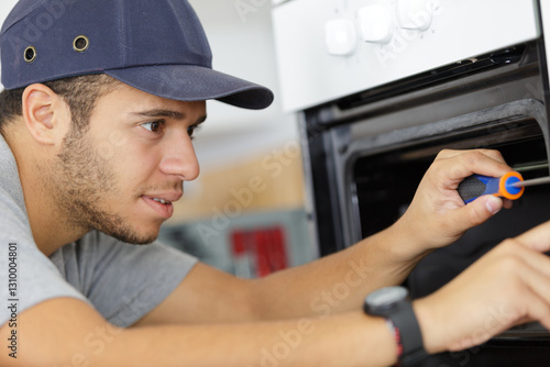 young male electrician fixing oven in kitchen photo