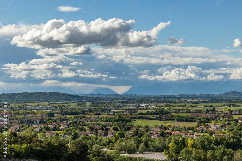 vista che si estende su un bellissimo ambiente misto urbano e naturale, che va dalla vicina pianura alle montagne lontane, nella regione Friuli Venezia Giulia, in Italia, con cielo nuvoloso, in estat