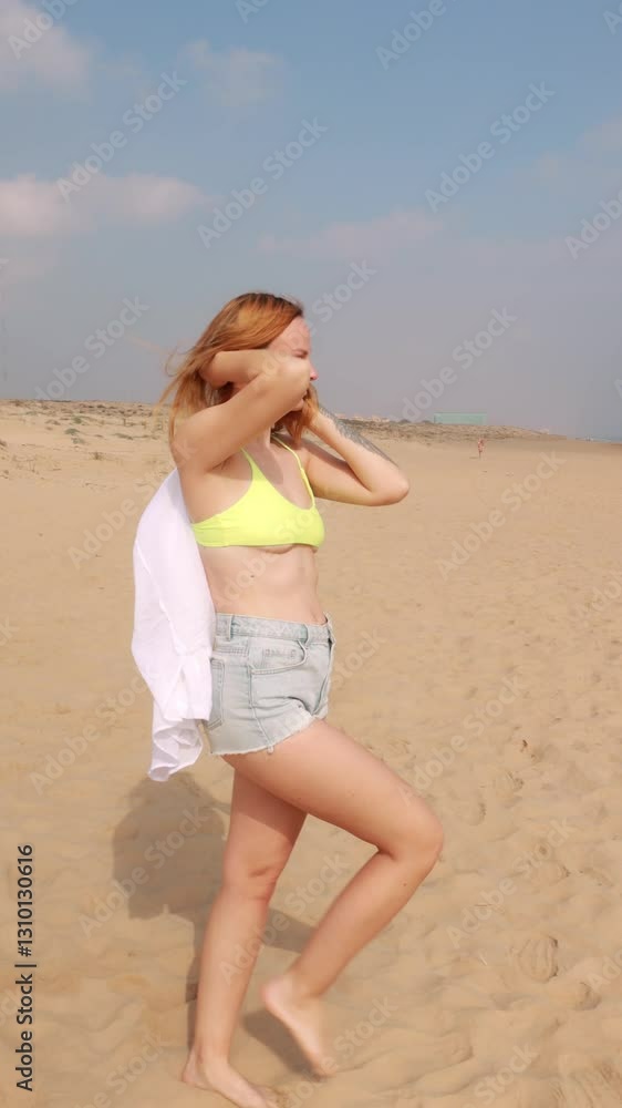 Vibrant female performer twirling white fabric, green bikini top and denim shorts, dancing freely near ocean waves under bright blue coastal sky Vibrant female performer twirling white fabric, green bikini top and denim shorts, dancing freely near ocean waves under bright blue coastal sky
