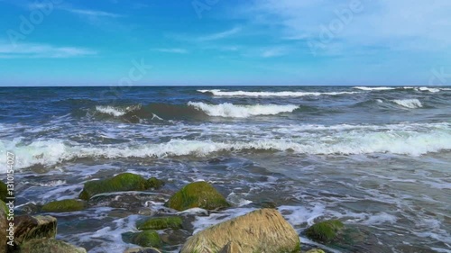 Waves with white foam are rolling and crashing over on the aged sea stones. Ocean, sea on clear weather.