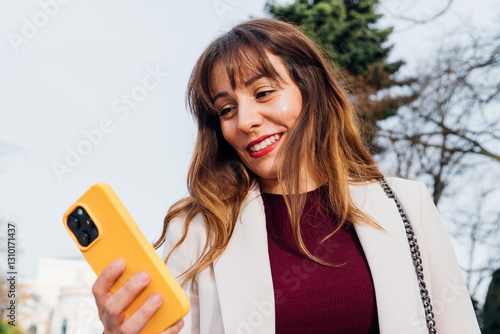 Slika na platnu Smiling businesswoman using smartphone outdoors in urban setting