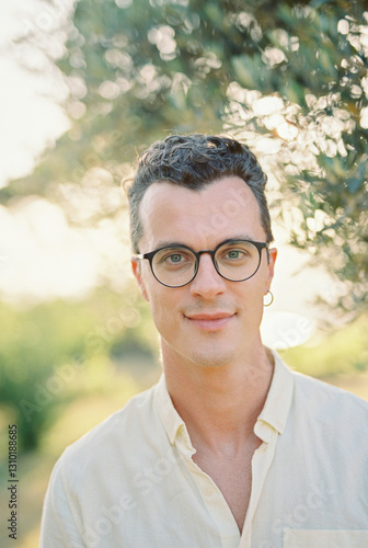 Young smiling man stands near a green tree in the garden. Portrait