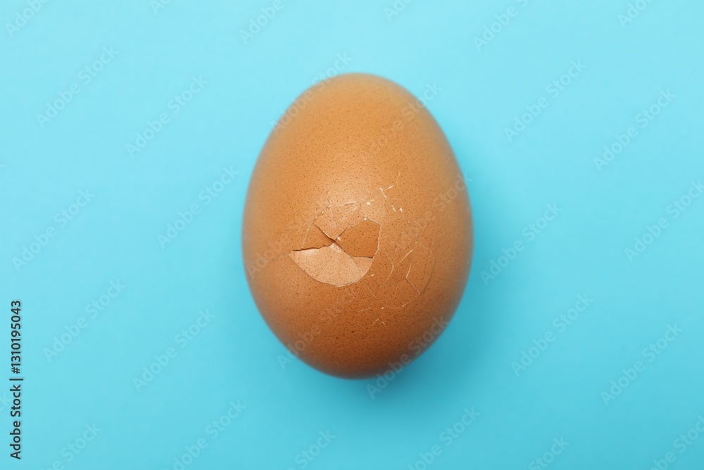 One egg with cracked shell on light blue background, top view One egg with cracked shell on light blue background, top view