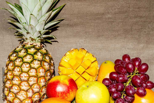 A vibrant mix of tropical fruits including pineapples, mangoes, bananas, and oranges, placed on a wooden table. The bright colors and healthy food vibe make it ideal for food photography and lifestyl photo