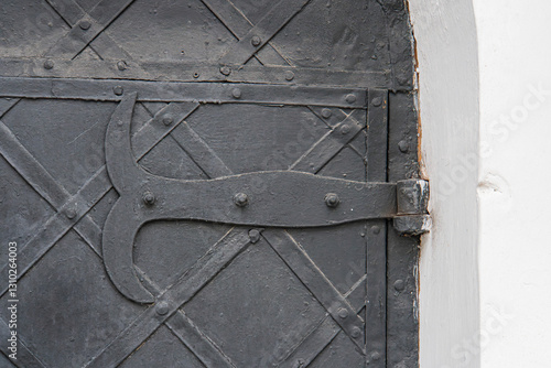 Close-up of ornate metal door with vertical slats, embossed patterns, and a stylized S on top right corner Weathered appearance, possible rusting, out-of-focus background hints at another door str photo