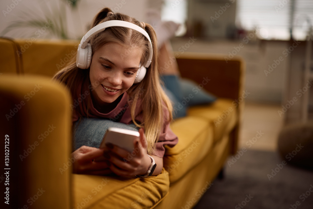 Obraz premium Happy teenager surfing the net on her mobile phone while relaxing on couch.